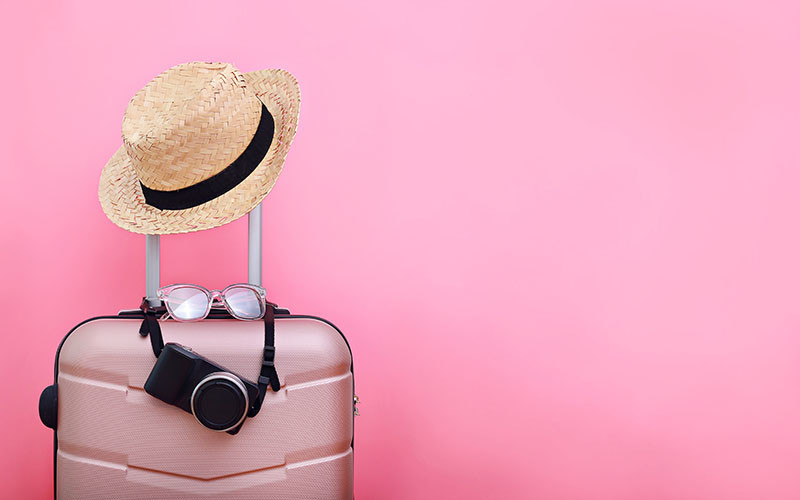 pink suitcase with beach hat, sunglasses and camera hanging on the handle