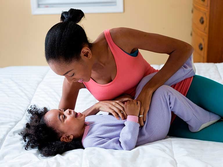 Mom tickling child in bed